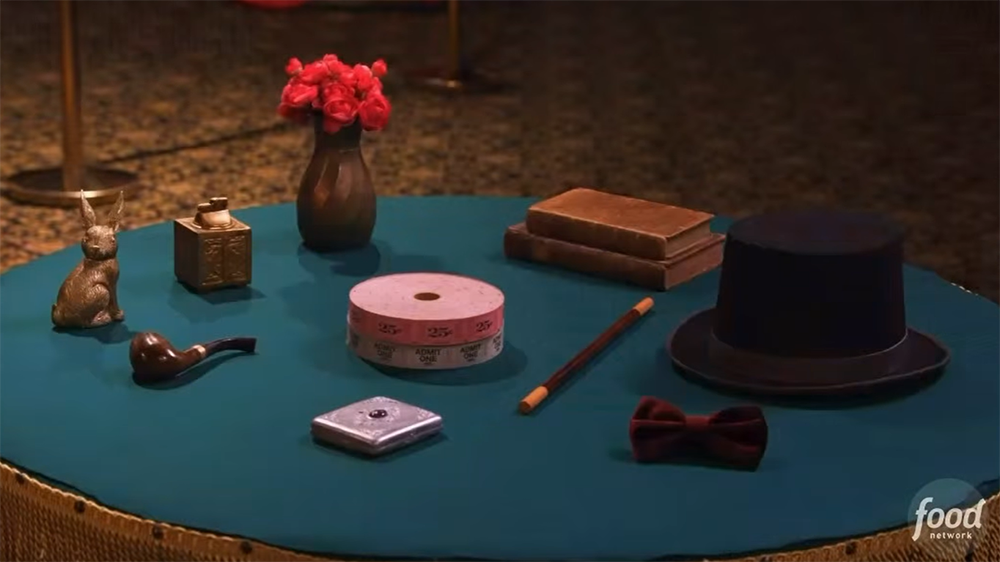 A round table with a brass rabbit, a lighter, a pipe, a vase of roses, a roll of tickets, a compact, a wand, books, a top hat, and a bow tie